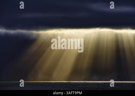 Dramatic rays of sunshine break through the dark clouds and illuminate the calm sea, Chile, South America Stock Photo