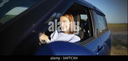 Woman smiling while driving a blue car under bright sunlight Stock Photo