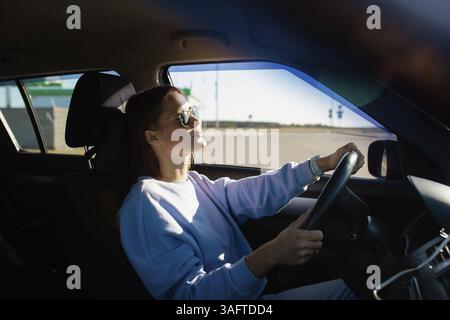 Woman driving and basking in sunlight, wearing sunglasses Stock Photo