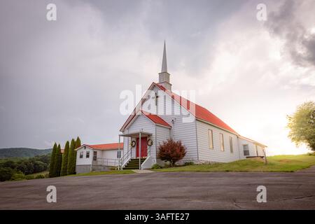 Sun breaking through the clouds behind a church on the top of a hill with a red roof. Stock Photo