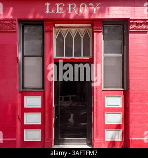 A striking red residential door is framed by sharp white stonework and topped with twin triangular windows, creating a bold and geometric facade in Ch Stock Photo