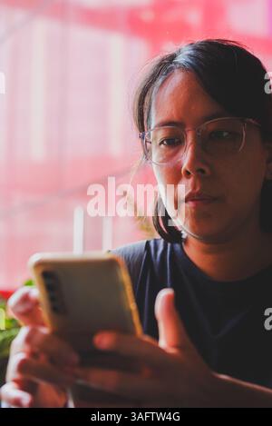The woman is sitting while looking at her smartphone. Stock Photo