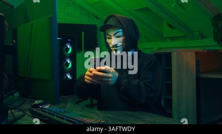 Lviv, Ukraine - June 03, 2024: Anonymous hacker smartphone monitor computer technology cyber crime thief masked man danger pointing finger no forbid Stock Photo