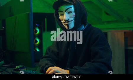 Lviv, Ukraine - June 03, 2024: Keyboard computer hacking man mask anonymous typing desktop pc looking at camera steal monitor database coding virus Stock Photo
