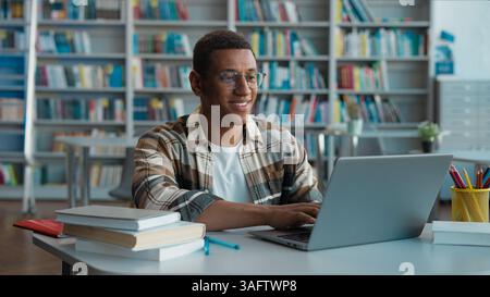 Happy African American man male guy student motivation smiling typing laptop e-learning project diploma studying learning high school computer gadget Stock Photo