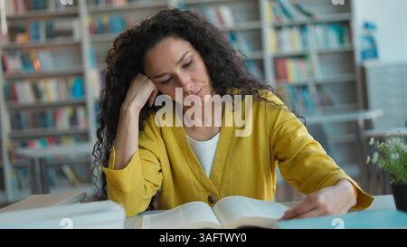 Tired Latino arabian woman sitting reading book studying knowledge exam preparation lesson lecture session student girl female library boredom Stock Photo