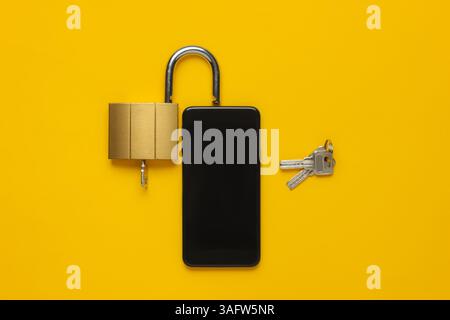 Protecting your smartphone’s personal data. Smartphone with keys lock on yellow background. Top view Stock Photo