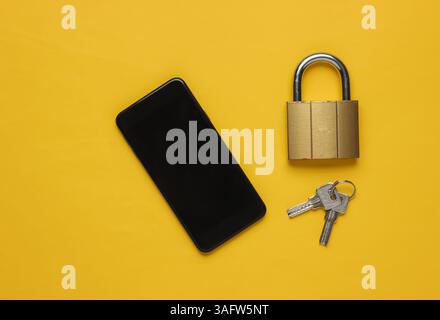 Protecting your smartphone’s personal data. Smartphone with keys lock on yellow background. Top view Stock Photo