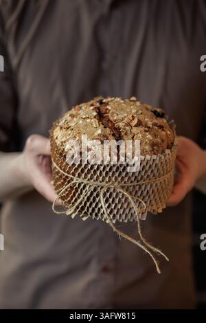 Man holding artisan Easter bread with almonds and sugar topping, wrapped in eco kraft paper for gifting. Stock Photo