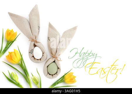 Easter eggs wrapped in a napkins folded like bunny ears with yellow tulips isolated on white background. Happy Easter concept. Top view. With space fo Stock Photo