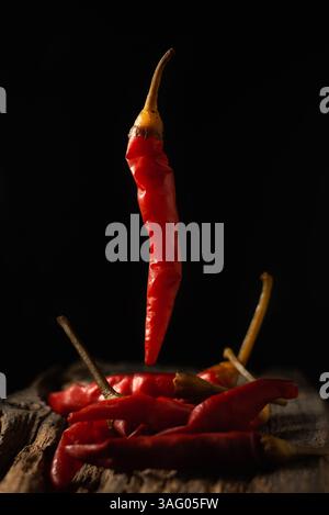 Red chili peppers hanging in the air on a black background. below there are still peppercorns on a wooden board. Levitation Stock Photo