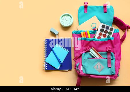 School backpack with different stationery supplies and alarm clock on beige background Stock Photo