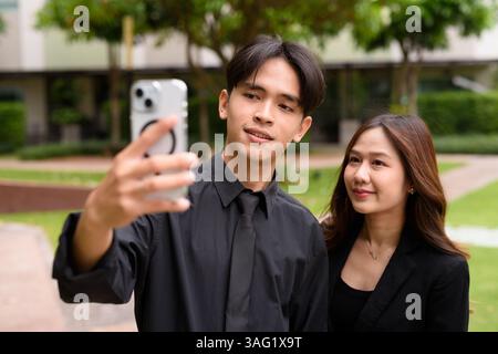 Portrait of young Asian couple wearing business uniform in park during summer Stock Photo