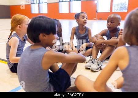 Sitting in gym, group of school diverse children talking and bonding together Stock Photo