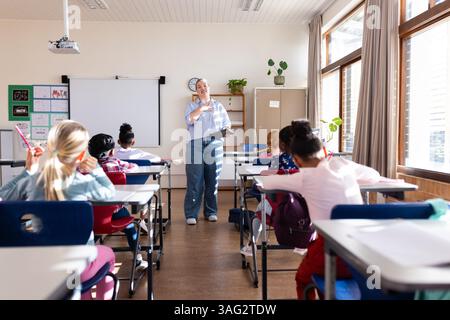 In school, female teacher instructing diverse group of students in classroom setting Stock Photo