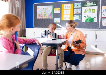 Helping african american boy with tablet in school, female teacher and another student watching Stock Photo
