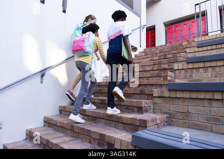 Diverse students with backpacks walking up stairs to school, heading to class Stock Photo
