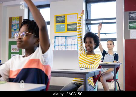 In school, diverse students raising hands in classroom, participating in lesson actively Stock Photo