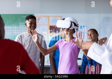 Using VR headset, students in school classroom exploring virtual reality together Stock Photo