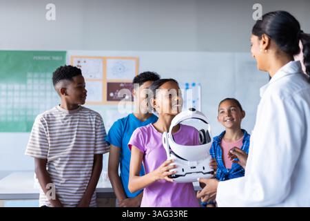 In school, students interacting with Indian female teacher while holding VR headset in classroom Stock Photo