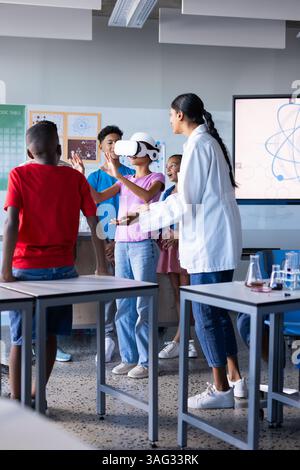 In school, students using VR headset in classroom with Indian female teacher guiding them Stock Photo