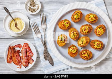 Deep fried deviled eggs with crispy coating of panko and parmesan, sprinkled with fresh chives and crumbled bacon on white plate on wooden table with Stock Photo
