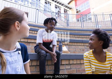In school, three diverse kids sitting on steps, talking and enjoying break time Stock Photo