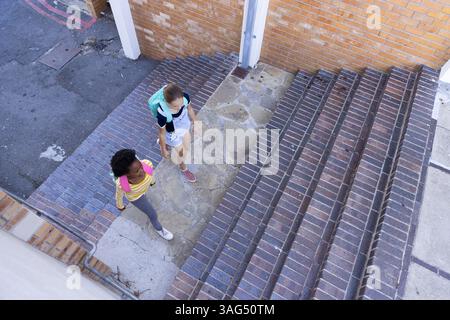 Walking up stairs, two school diverse girls with backpacks heading to class Stock Photo