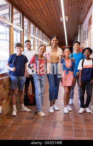 Indian female teacher standing with group of students in school hallway, all smiling Stock Photo