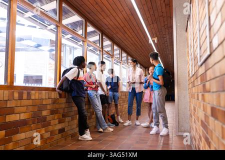 In school hallway, Indian female teacher talking with group of students, engaging in discussion Stock Photo