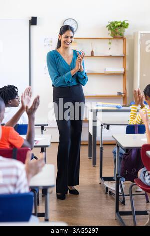 In school, Indian female teacher clapping and smiling while students applaud in classroom Stock Photo
