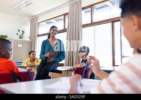 In school, Indian female teacher holding tablet and engaging with students in classroom Stock Photo