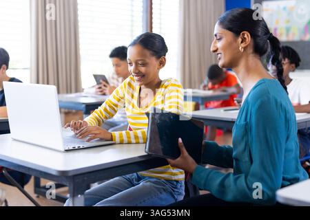 Female Teacher Helping Pupil Using Computer In Classroom Stock Photo ...