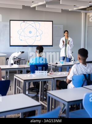 Explaining science concept in school, indian female teacher with students using microscopes Stock Photo