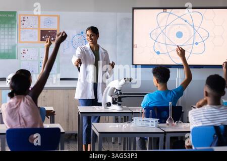 In school, Indian female teacher engaging students in science lesson with microscope and screen Stock Photo