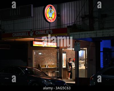 View from outside a Chargrill Charlie's chicken shop at night, with bright yellow and red illuminated signage Stock Photo