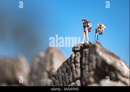 Miniature backpackers standing on top of a mountain under a clear blue sky, enjoying the view and celebrating their achievement Stock Photo