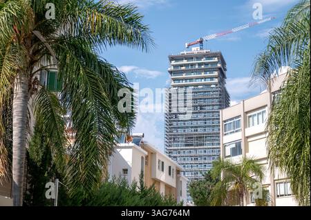 Tower crane working on modern skyscraper rising above residential buildings in Limassol, Cyprus, showcasing urban development and growth Stock Photo