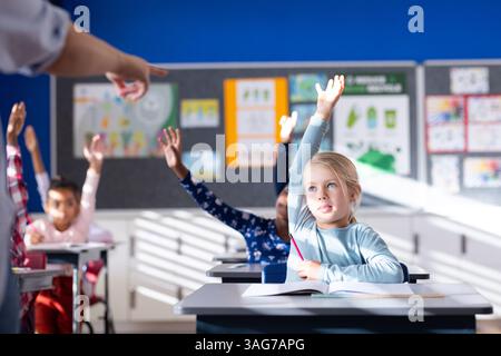 In school, diverse students raising hands in classroom, participating in lesson Stock Photo