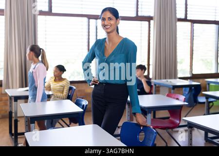In school, Indian female teacher standing confidently in classroom with students in background Stock Photo