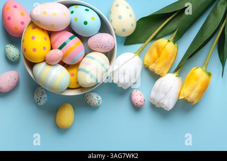 Happy Easter. Colorful easter painted eggs and white and yellow tulips over blue background Stock Photo