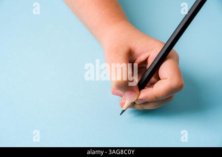 Left hand holding a ballpoint pen on an open notebook on a blue background Stock Photo