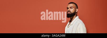 Bearded man stands confidently, showcasing stylish fashion against vibrant orange hues. Stock Photo