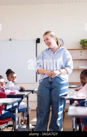 In school, female teacher smiling and engaging with diverse students in classroom setting Stock Photo