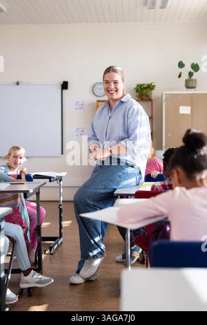 In school, female teacher smiling and engaging with diverse students in classroom setting Stock Photo