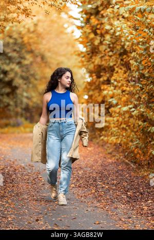 Woman walking in park on a beautiful sunny day of autumn. Young woman enjoying time outdoor on an autumn alley Stock Photo