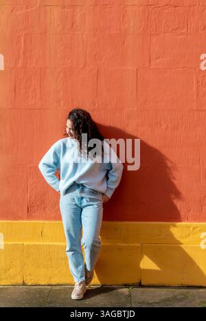 Minimalism image with a young woman enjoying the morning sun in front of  a orange wall on a sunny day of October. Stock Photo