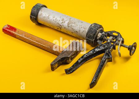 A hammer, caulking gun, and tube of sealant are displayed on a vibrant yellow background, illustrating essential tools for various construction tasks. Stock Photo