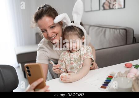 A mother and her daughter are joyfully enjoying a festive crafting session, making bunny ears and painting Stock Photo