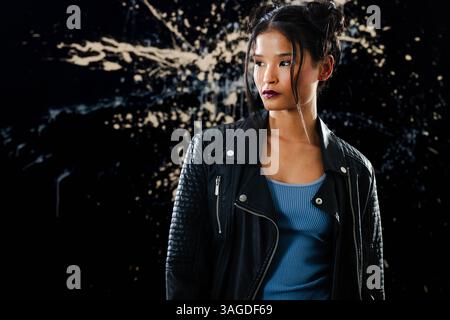 Confident woman in leather jacket standing against artistic paint splatter backdrop. Fashion, style, confidence, expression, background, edgy Stock Photo